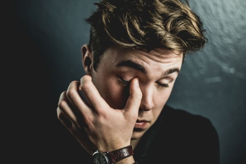 Exhausted young man rubbing his eyes due to high cortisol levels and chronic fatigue