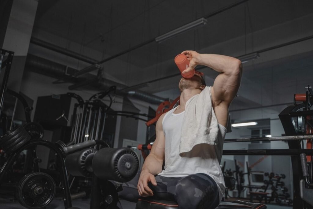 Muscular athlete drinking from a shaker bottle in a gym after a workout, representing muscle recovery in Chicago Illinois