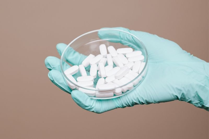 Gloved hand holding a glass petri dish filled with white Pharmacore Laboratories LTD supplement tablets